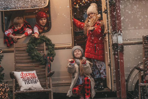 Children celebrating Christmas and New Year winter holidays season outdoor waiting Santa. Kids joyful spending time together near Xmas camper trailer rejoices at first snow enjoying childhood - Foto, immagini