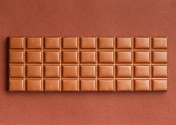 Kahverengi arka planda koca bir çikolata, üst manzara. Sütlü çikolata izole. - Fotoğraf, Görsel