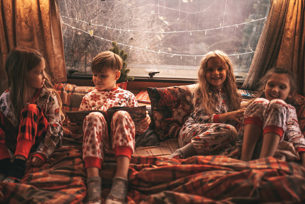 Children celebrating Christmas and New Year winter holidays season in camper. Active kids spending time together grimace having fun and reading book at Xmas camper trailer enjoying childhood - Photo, Image