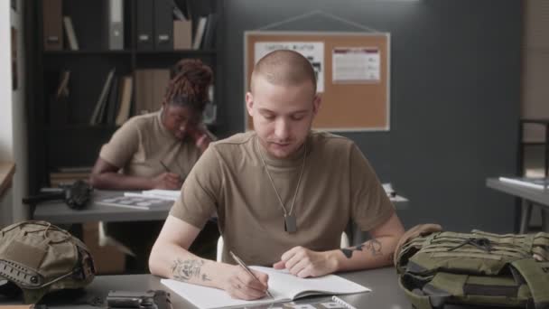 Portrait moyen de cadet caucasien sérieux avec des tatouages étudiant pendant la classe de service militaire, puis regardant la caméra au collège - Séquence, vidéo