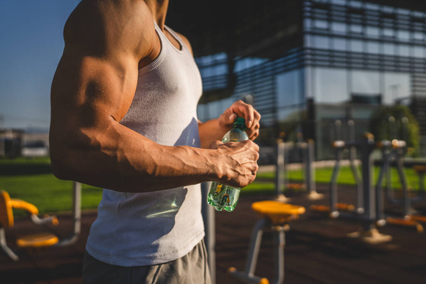 egy férfi kaukázusi férfi sportoló tartsa műanyag palack víz nyílás és felkészülnek, hogy igyon, miközben edzés szabadtéri napsütéses nap hidratáció és az egészséges életmód koncepció másolás tér - Fotó, kép