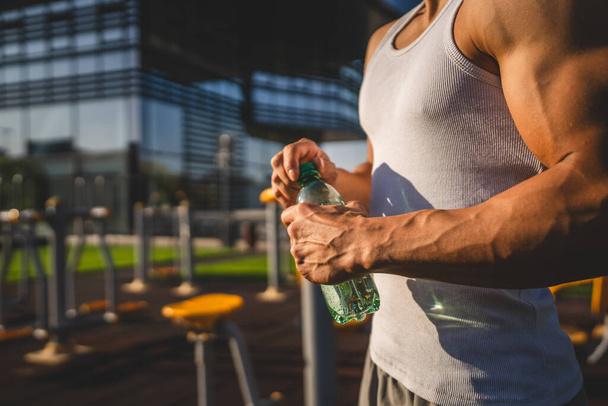one man caucasian male athlete hold plastic bottle of water opening and prepare to drink while training outdoor in sunny day hydration and healthy lifestyle concept copy space - Photo, Image