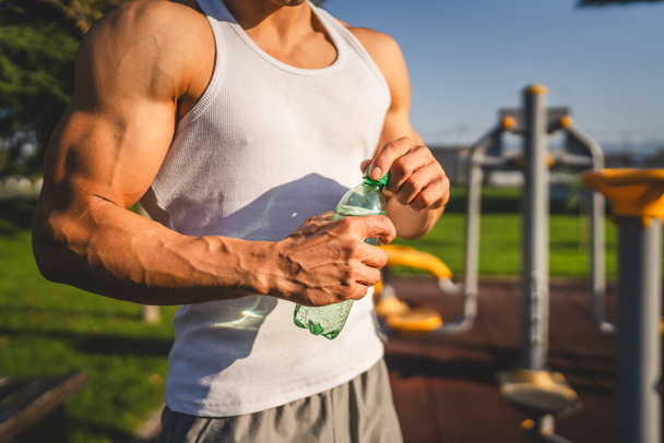 Beyaz tenli bir erkek sporcu plastik su şişesini açık tutuyor ve açık havada güneşli su ve sağlıklı yaşam tarzı konsepti fotokopi çekerken içmeye hazırlanıyor. - Fotoğraf, Görsel