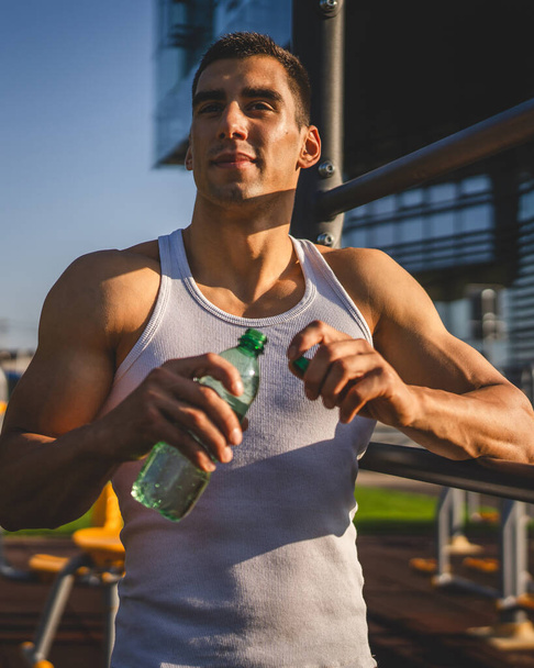 yksi mies valkoihoinen mies urheilija pitää muovipullo vettä avaamalla ja valmistautua juoda harjoitellessaan ulkona aurinkoisena päivänä nesteytys ja terveiden elämäntapojen käsite kopioi tilaa - Valokuva, kuva