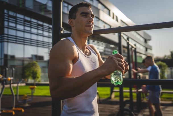 un uomo atleta maschio caucasico tenere bottiglia di plastica di apertura dell'acqua e prepararsi a bere durante l'allenamento all'aperto in giornata di sole idratazione e stile di vita sano concetto di spazio copia - Foto, immagini