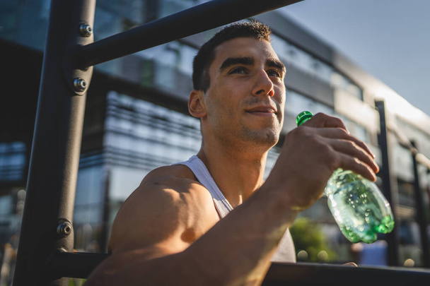 een man Kaukasische mannelijke atleet houden plastic fles water openen en voor te bereiden om te drinken tijdens de training buiten in zonnige dag hydratatie en gezonde levensstijl concept kopiëren ruimte - Foto, afbeelding