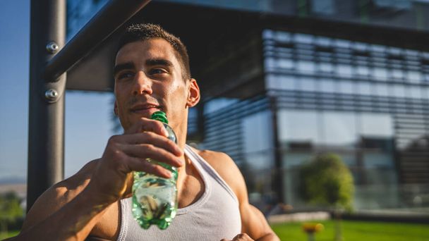 один чоловік білий спортсмен тримає пластикову пляшку відкриття води і готується до пиття під час тренування на відкритому повітрі в сонячний день гідратації і здорового способу життя концепції копіювання простору - Фото, зображення