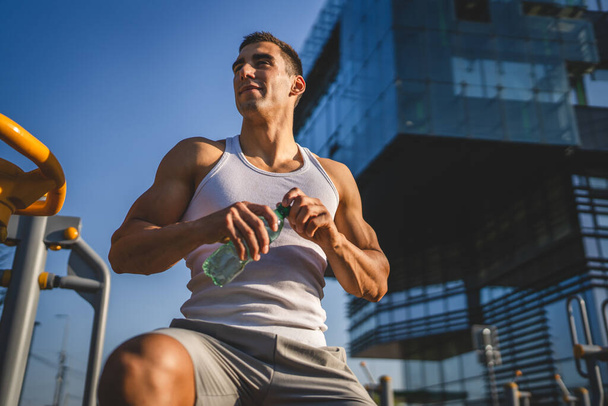 Beyaz tenli bir erkek sporcu plastik su şişesini açık tutuyor ve açık havada güneşli su ve sağlıklı yaşam tarzı konsepti fotokopi çekerken içmeye hazırlanıyor. - Fotoğraf, Görsel