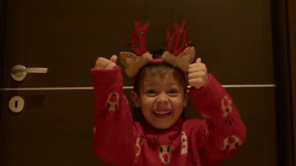 Pulgares arriba. Emocionado niño feliz en jersey de Navidad y cuernos de reno expresando con entusiasmo sus gustos hacia los regalos. Imágenes de alta calidad 4k - Metraje, vídeo