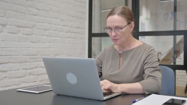 Opgewonden senior oude vrouw viert succes op laptop in kantoor - Video