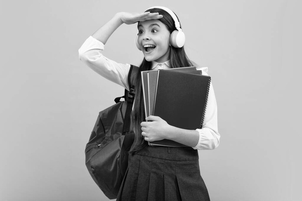 Iskoláslány, tinédzser lány fülhallgatóban könyveket tart a kék elszigetelt stúdió hátteréről. Iskolai és zenei nevelési koncepció. Vissza az iskolába. - Fotó, kép