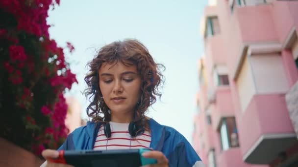 Fiatal nő játszik Nintendo kapcsoló konzol séta nyári utcában közelről. Dühös göndör lány elégedetlen videojáték hiba nyomja gombokat. Komoly tini összpontosított videojáték kézi vezérlő. - Felvétel, videó