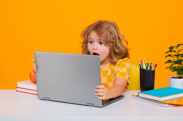 Izgalmas iskolás gyerek laptoppal. Iskola gyermek portré elszigetelt sárga stúdió háttér. Kisfiú az általános iskolából. Tanulj a tanulásból. Okos iskolás fiú tanulás - Fotó, kép