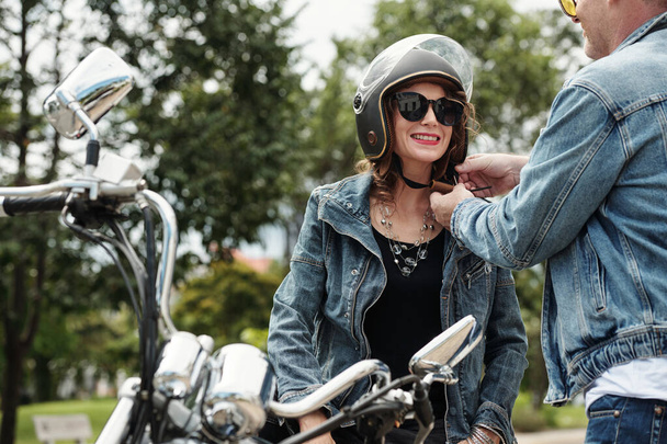 車に乗る前にオートバイのヘルメットを取るガールフレンドを助けるカーリングマン - 写真・画像