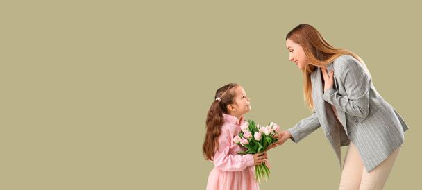 Cute little girl greeting her mother with tulips on green background with space for text - Photo, Image