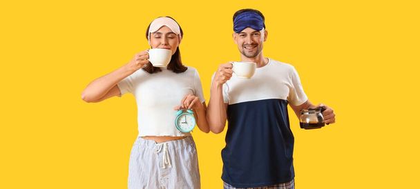 Молода пара з кавою і будильником на жовтому фоні - Фото, зображення