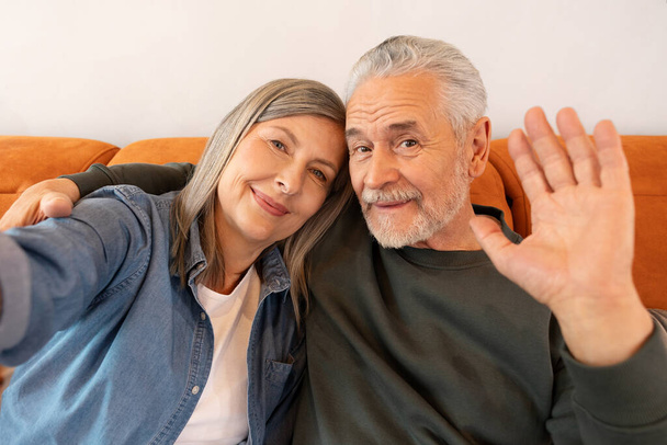Happy elderly couple smiling on sofa, embracing and looking at camera. Couple taking a selfie. Happy and positive emotions - Photo, Image