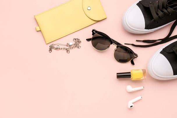 Samenstelling met stijlvolle zonnebril, moderne oortjes, sneakers en nagellak op roze achtergrond - Foto, afbeelding