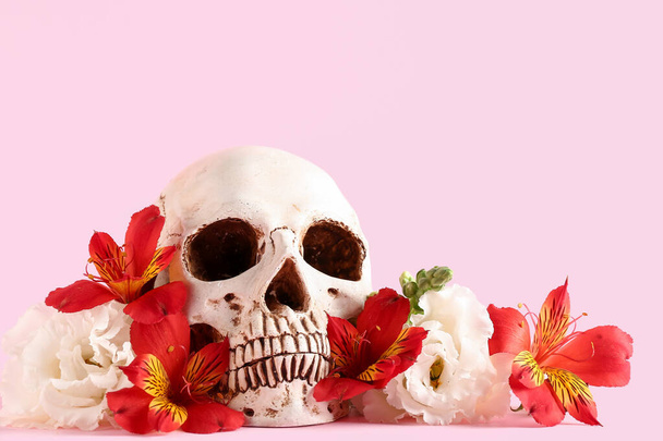 Menselijke schedel met mooie bloemen op roze achtergrond, close-up - Foto, afbeelding