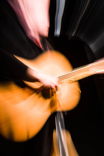 Dit beeld vangt de levendige energie van een gitarist in beweging, de snelle beweging van het tokkelen vervaagt in lichtstrepen tegen het gitaarlichaam. De dynamische aard van het schot brengt de - Foto, afbeelding