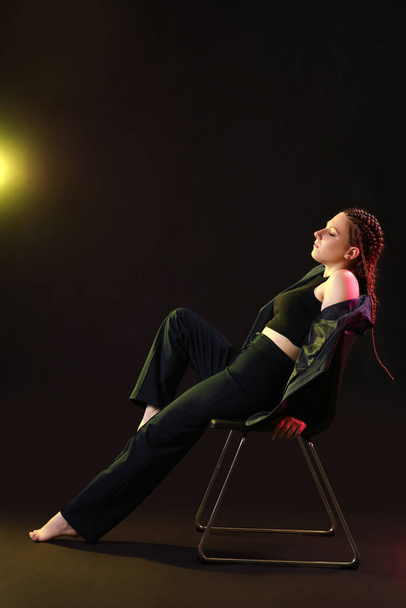 Mujer joven con rastas sentada sobre fondo oscuro - Foto, imagen