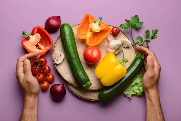 Homme avec planches en bois, légumes frais et verdure sur fond violet - Photo, image