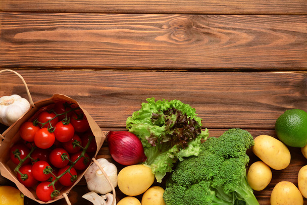 Бумажный пакет с помидорами и свежими овощами на деревянном фоне - Фото, изображение