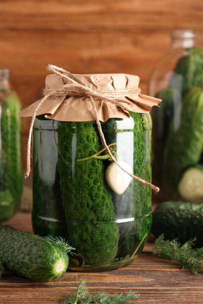 Potje met komkommers in blik op houten ondergrond - Foto, afbeelding