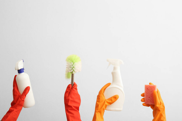 Manos femeninas en guantes de goma que sostienen los suministros de limpieza sobre fondo beige - Foto, Imagen