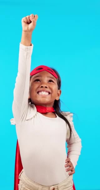 Mädchen mit Lächeln, Superheld und erhobener Hand zum Fliegen, Spielen und Fantasieren mit lustigen Kostümen und Mut im Studio. Super Power, Kinder Cosplay und Kind in Umhang, Maske und Heldenfigur Spiele auf blauem Hintergrund - Filmmaterial, Video