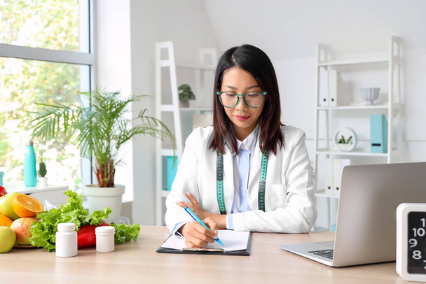 Female Asian nutritionist working at table in office - Photo, Image