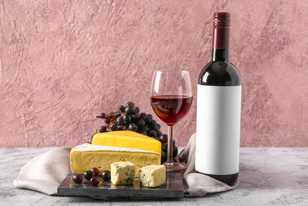 Дошка зі смачним сиром, виноградом, пляшкою та келихом вина на сірому фоні - Фото, зображення