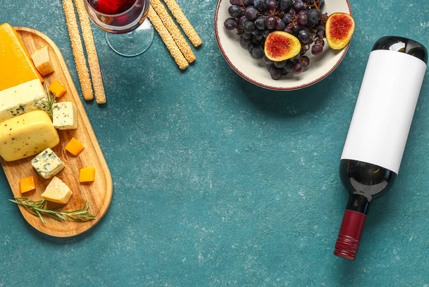 Вкусный сыр, гриссини, фрукты, бутылка и бокал вина на зеленом фоне - Фото, изображение