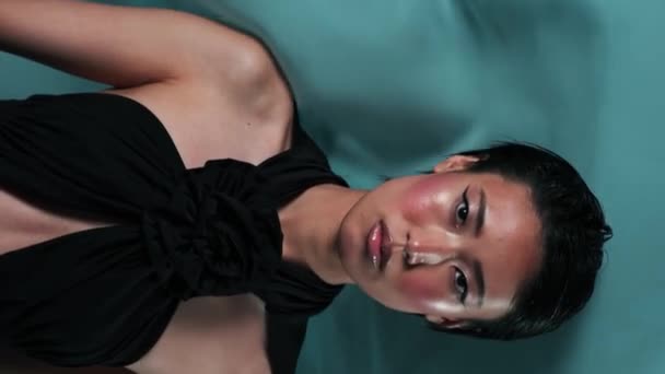 Studio verticaal portret van jong Aziatisch model met heldere make-up. Om haar heen fladderen stukjes zijde in de wind. - Video
