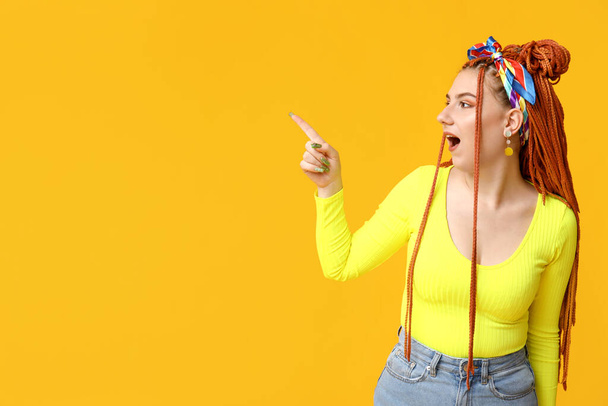 Retrato de una hermosa joven con rastas apuntando a algo sobre fondo amarillo - Foto, Imagen
