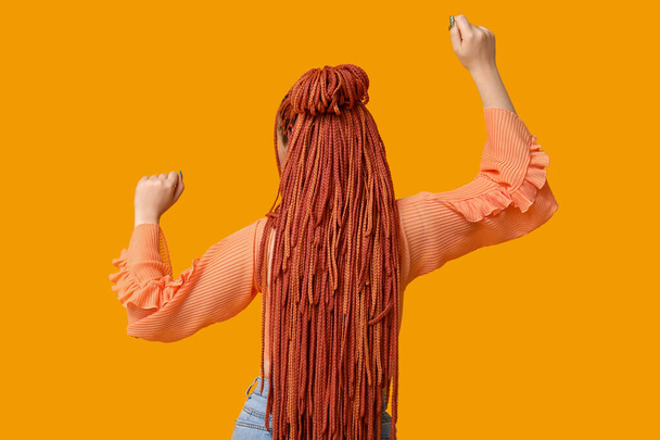 Mladá žena s dredy na oranžovém pozadí, zadní pohled - Fotografie, Obrázek