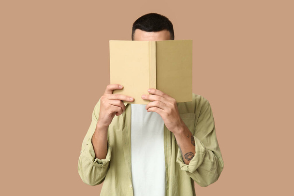 Giovane uomo che copre il viso durante la lettura del libro su sfondo beige - Foto, immagini