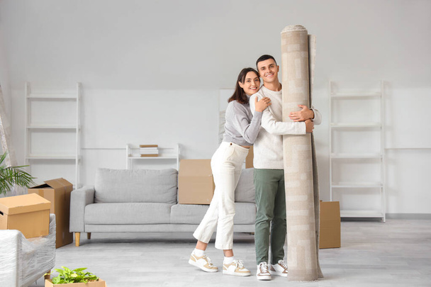 Heureux jeune couple avec tapis roulé dans la chambre le jour du déménagement - Photo, image