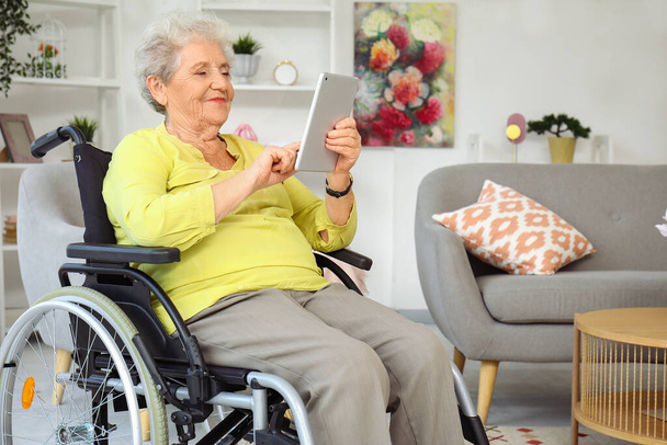 Donna anziana in sedia a rotelle utilizzando tablet computer a casa - Foto, immagini