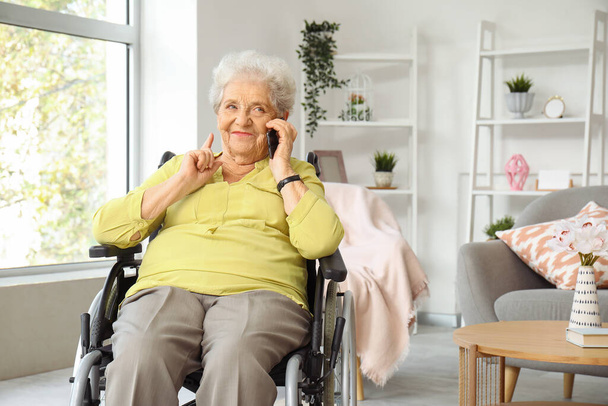 Mujer mayor en silla de ruedas hablando por teléfono móvil en casa - Foto, Imagen