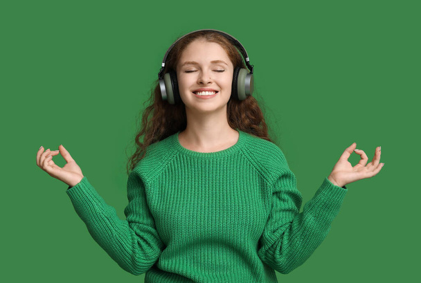 Portret van een ontspannen jonge vrouw mediteren tijdens het luisteren naar muziek op groene achtergrond - Foto, afbeelding