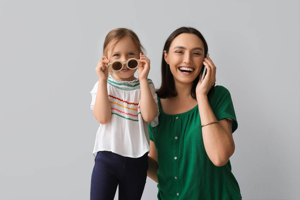 Kaunis äiti hänen söpö pieni tytär puhuu matkapuhelimella harmaalla taustalla - Valokuva, kuva