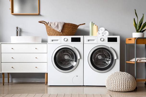 Çamaşır makineleri, hasır sepeti ve temizlik malzemeleriyle çamaşır odasının içinde. - Fotoğraf, Görsel