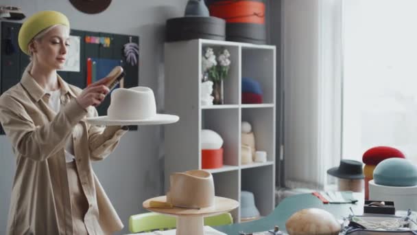 Retrato de sombrerera caucásica hembra mirando a la cámara y sonriendo mientras trabajaba en su taller - Metraje, vídeo