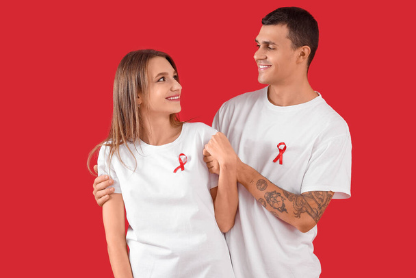 Молодой человек и женщина с красными лентами на цветном фоне. Всемирный день борьбы со СПИДом - Фото, изображение