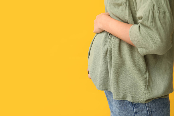 Беременная женщина на жёлтом фоне, крупный план - Фото, изображение