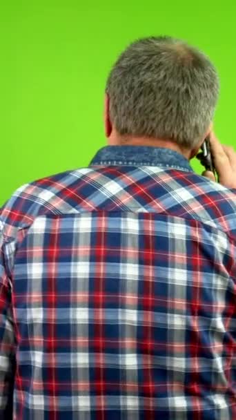 Achteraanzicht van een oudere man in casual kleding die met een mobiele telefoon praat. Volwassen persoon voert gesprekken met behulp van zijn smartphone en loopt weg van de camera. Groen scherm, chroma toets. - Video