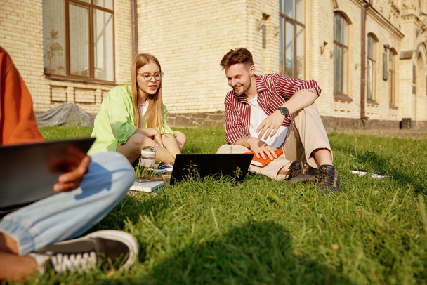 Studenti vysokých škol studují venku, diskutují a připravují se na zkoušky na trávníku univerzitního kampusu. Happy interracial žáci brainstorming na projektu společně pomocí moderní technologie - Fotografie, Obrázek