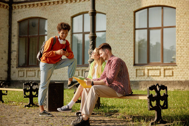 Университетские друзья отдыхают на улице. Молодые международные люди мило общаются, делятся новостями в кампусе - Фото, изображение