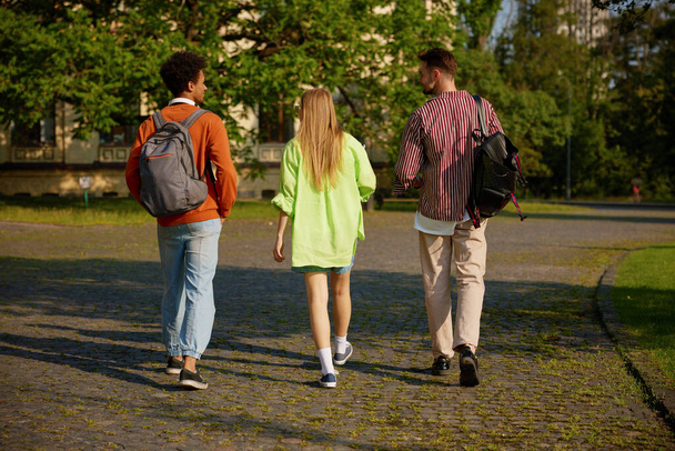 Ryhmä opiskelijoita reppuineen kävelee yhdessä kampuksen tietä pitkin aamutunnille. Koulutuksen käsite - Valokuva, kuva